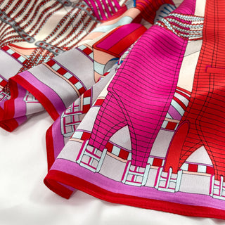 Luxurious silk scarf with geometric city maze pattern in vibrant magenta, red, light beige and grey, showcasing its lustrous texture and elegant design.
