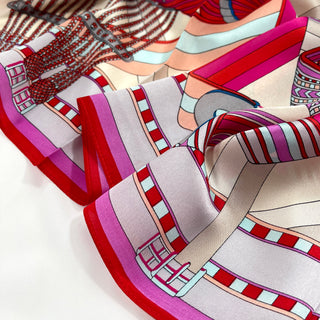 Silk scarf with geometric city maze pattern in vibrant magenta, red, ash grey, and light beige, showcasing luxurious fabric texture and edging.