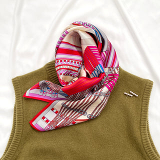 Magenta City Maze silk scarf with geometric pattern in vibrant pink, red and beige tones, elegantly draped on an olive green sweater
