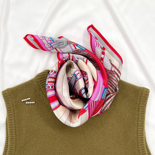 Luxurious Magenta City Maze silk scarf with geometric patterns in red, pink, blue and beige tones, elegantly draped on olive green sweater
