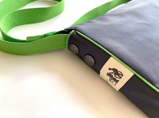 Recycled crossbody bag in gray with bright green strap and trim, featuring decorative metal buttons and a canvas tag with bicycle logo