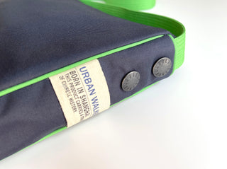 Navy blue recycled crossbody bag with bright green trim, Urban Walker brand tag, and metal button details, showcasing eco-friendly design