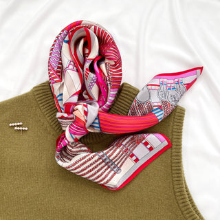 Luxurious Magenta City Maze silk scarf with geometric patterns in red, pink and beige, elegantly draped on olive green knitwear against white fabric.