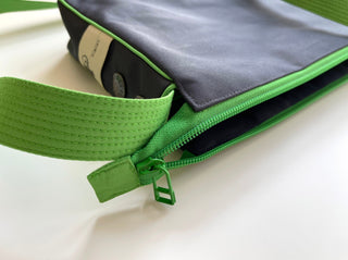 Recycled crossbody bag in dark gray with bright green trim, zipper, and strap, featuring YKK hardware and product tag detail