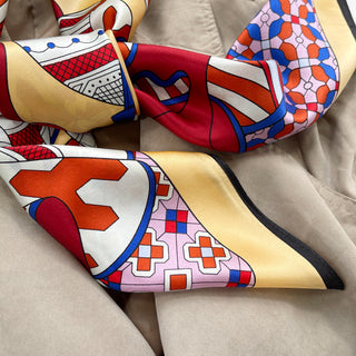 Luxurious 90cm silk scarf featuring medieval carnival pattern with light yellow, red, and blue geometric designs on soft fabric texture