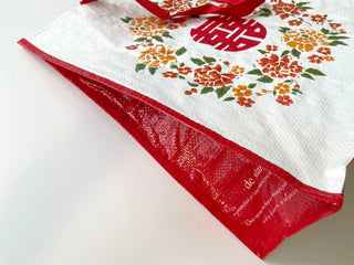 White shopping tote with vibrant orange and red floral pattern, red Chinese character in circle, red trim and handles, made from recycled plastic bottles
