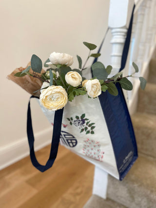 Vintage Chinese character tote bag with navy blue sides and handles, decorated with floral patterns, filled with cream-colored roses and greenery