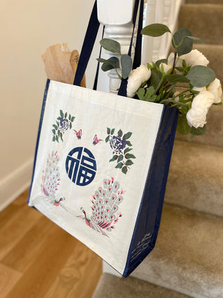 Vintage ethnic tote bag with navy trim featuring peacocks, flowers, and Chinese Fu character, filled with white flowers and greenery