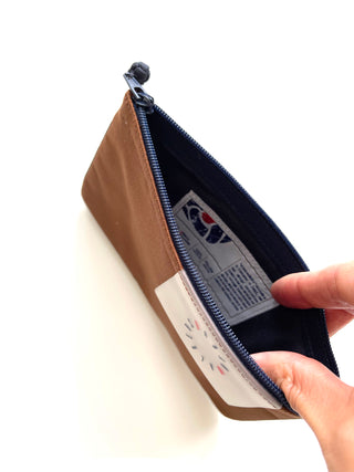 Open brown recycled RPET zipper wallet with navy blue lining, decorative handmade button detail, and brand tag visible inside the compact pouch