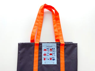 Recycled large tote bag in dark navy with bright orange handles and a light blue label featuring bag icons, displayed on white background