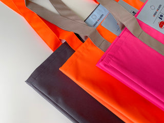 Three recycled RPET large tote bags in vibrant colors - charcoal gray, neon orange, and hot pink - with tan handles and neatly finished edges