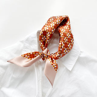Silk bandana with orange, pink and gold retro geometric mosaic pattern, tied elegantly around a white collar, showcasing its luxurious sheen