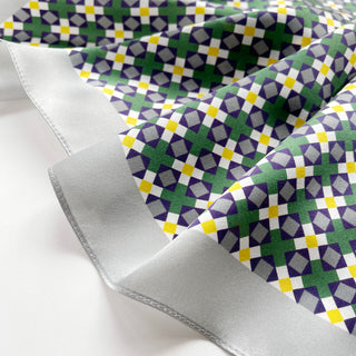 Silk scarf with geometric mosaic pattern in green, purple, yellow and white with silver border, showing the fabric's luxurious sheen and texture.