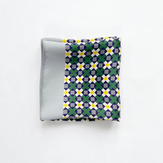 Folded silk bandana with geometric mosaic pattern featuring green, purple, yellow and white shapes, with light gray border edge