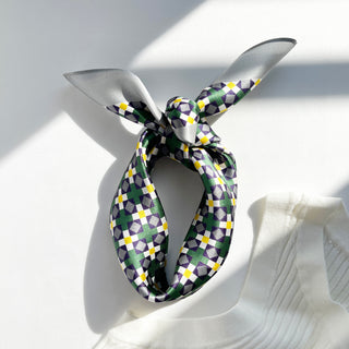 Silk bandana tied in a knot featuring geometric mosaic pattern in green, purple, yellow and white, displayed on light background