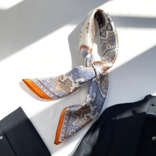 Luxurious silk scarf with blue, orange and beige baroque pattern elegantly tied as a neckerchief against formal attire in natural light