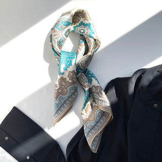 Elegant silk scarf with turquoise, beige and cream baroque pattern, loosely tied on navy shirt in natural lighting, showcasing luxurious texture