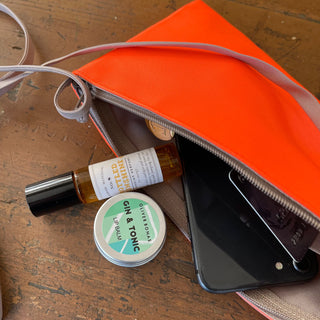 Bright orange crossbody phone wallet with gray trim showing contents including smartphone, lip balm, and small perfume bottle on wooden surface