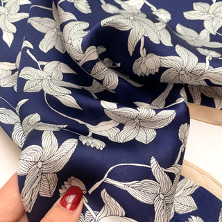 Navy blue silk scarf with elegant white floral pattern, showing soft fabric texture and delicate botanical design perfect for versatile styling.