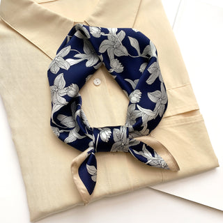 Navy blue silk bandana scarf with white floral pattern tied elegantly around collar of cream blouse, showcasing versatile styling