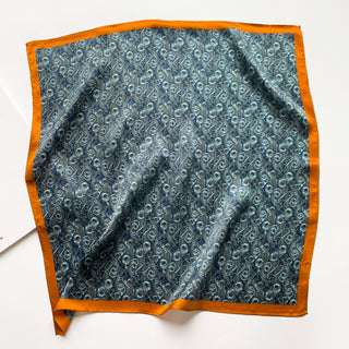 Square silk neckerchief with deep blue paisley wave pattern and vibrant orange border, displayed flat showing shimmering texture