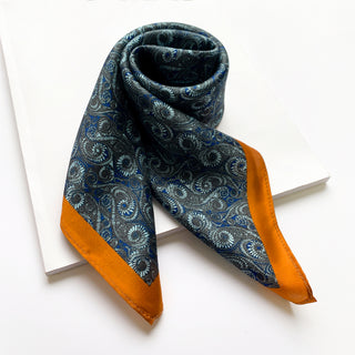 Deep blue silk neckerchief with circular wave pattern and orange trim border, elegantly folded on white surface showing its smooth texture
