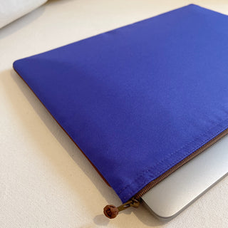 Vibrant blue recycled laptop sleeve with piped edges and YKK zipper, partially containing a MacBook on cream background