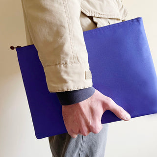 Vibrant purple minimalist laptop sleeve made from recycled materials, being held by a person wearing a beige jacket, featuring YKK zipper