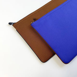 Two minimalist RPET laptop sleeves for MacBook, one brown and one vibrant blue, featuring traditional Chinese button detail and YKK zippers