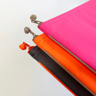 Close-up of vibrant recycled laptop sleeves with YKK zippers and handmade button details, shown in bright pink, orange, and black colors.
