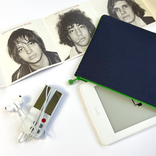 Navy blue iPad case with bright green zipper shown with a Kindle e-reader, earbuds, and music magazine on white background