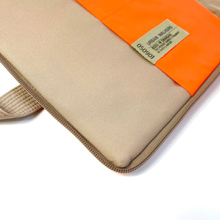 Beige recycled laptop briefcase with bright orange accent band, zippered edge, and Urban Walkers label, showing corner detail and quality piping.
