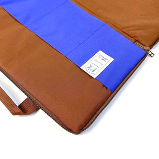 Open waterproof laptop briefcase in brown and vibrant blue, showing interior pocket design, YKK zipper, and label tag, made from recycled RPET material.