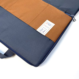 Interior view of navy blue recycled laptop briefcase with tan pocket, authentication label, and smooth zipper closure for 13-14 inch devices.