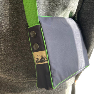 Recycled crossbody bag in gray with bright green trim, featuring decorative bicycle patch and metal buttons on adjustable green strap.