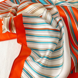 Silky navy and orange striped bandana scarf with teal blue accents, draped to showcase lustrous fabric texture and vibrant color pattern