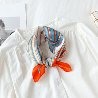 Navy and orange striped silk bandana scarf tied neatly with vibrant orange tips, displayed on white blouse background