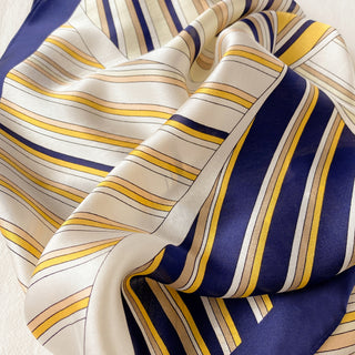Silk scarf with navy blue, orange, and cream striped pattern, elegantly draped to showcase its lustrous texture and sunburst design.