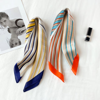 Two silk square bandanas displaying striped patterns - one with navy and yellow stripes, another with orange and blue sunburst stripes, on white background