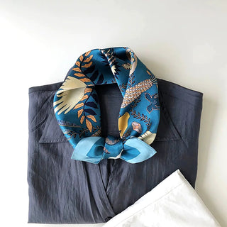 Dusty blue silk bandana scarf with tarot-inspired mystical patterns and gold accents, tied elegantly around navy blouse collar