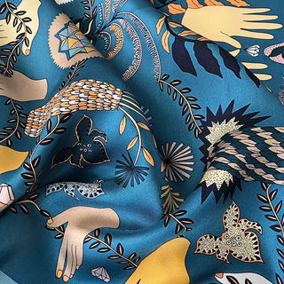 Dusty blue silk scarf with mystical tarot-inspired design featuring hands, leaves, geometric shapes and abstract patterns in gold, orange and navy