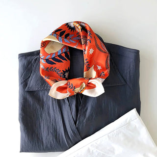 Vibrant orange silk bandana scarf with mystical Tarot-inspired patterns and blue foliage designs, styled on a navy blue shirt