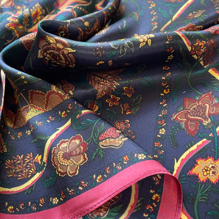 Navy blue silk scarf with vintage floral pattern featuring gold, red, and green botanical designs with pink trim, showing luxurious fabric texture