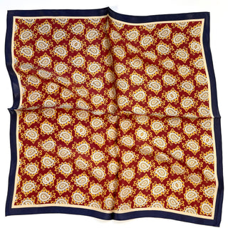 Square silk neckerchief with rich red background, gold and cream paisley pattern, and navy blue border, displayed flat showing luxurious texture