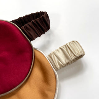 Luxury double-sided silk sleep mask featuring rich burgundy and caramel gold colors with brown and cream elastic bands, displayed on white background.