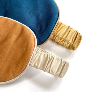 Luxurious double-sided silk sleep mask featuring rich blue and caramel colors with elegant golden trim and comfortable elastic bands
