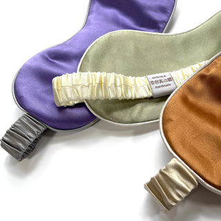 Luxury silk sleep masks in purple, sage green, and copper tones with elastic bands, featuring 100% silk label, arranged on white background