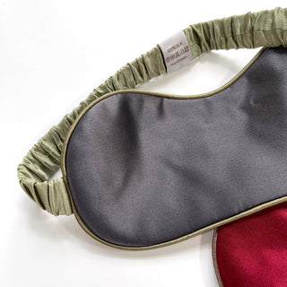 Luxury double-sided silk sleep mask featuring deep red and gray surfaces with sage green elastic band and trim, showing 100% silk label