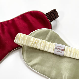 Double-sided luxury silk sleep masks showing sage green and burgundy colors with elastic bands and 100% silk label against white background