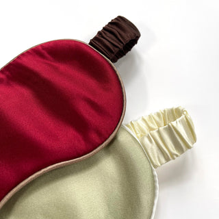 Luxurious double-sided silk sleep mask featuring deep red and light cream colors with contrasting elastic bands against white background